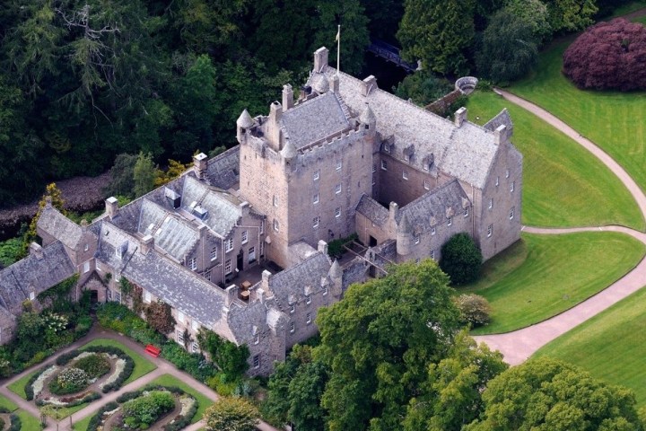 Aerial view of a historic stone castle surrounded by gardens and trees.