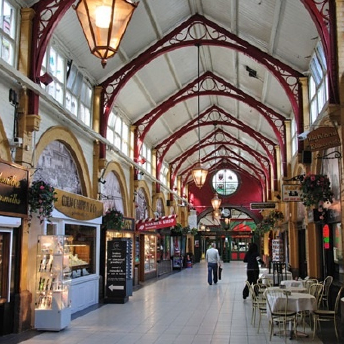Indoor market with arched ceiling, shops, and cafes; people walking on tiled floor.