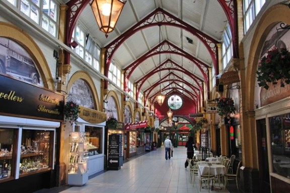 Indoor market with arched ceiling, shops, and cafes; people walking on tiled floor.