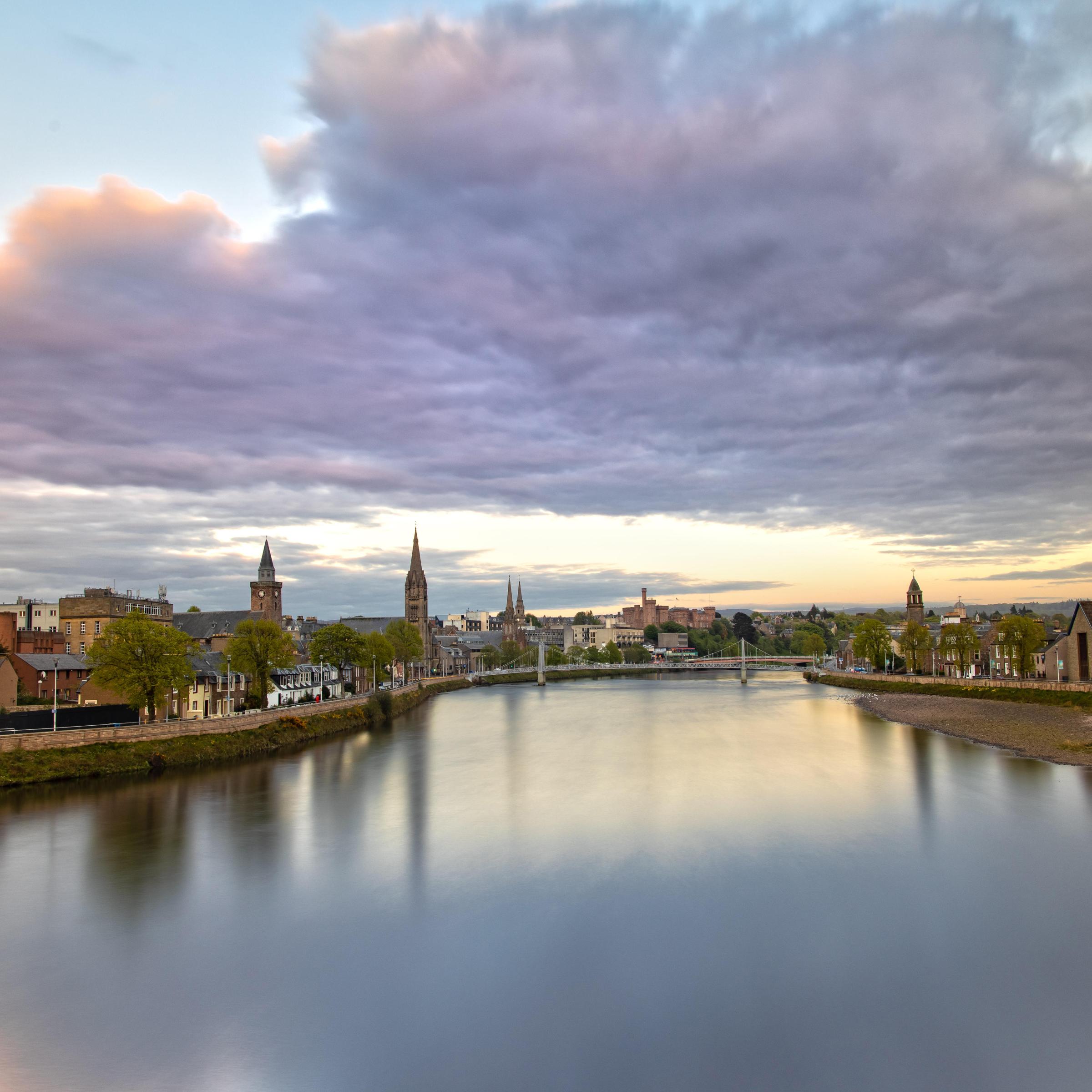 Scenic view of a river with a town, cloudy sky, and sunset light.